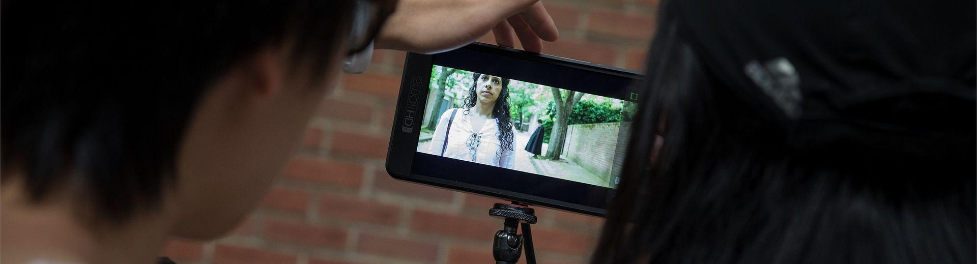 Students watch the shooting of a film on a small monitor.